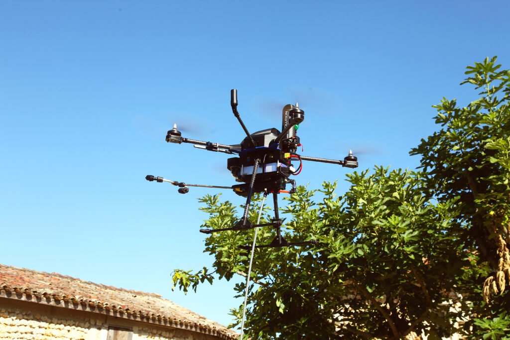 Drone de traitement Eco Drones en vol au-dessus d’une toiture en tuiles, lance de pulvérisation et tuyau visibles