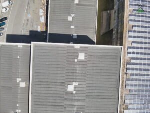 Vue aérienne verticale d'une toiture industrielle en plaques ondulées grises, ligne de vie et lanterneaux