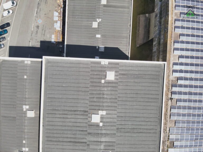 Vue aérienne verticale d'une toiture industrielle en plaques ondulées grises, ligne de vie et lanterneaux