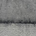 Mur en crépi gris : partie haute encrassée et microfissurée, partie basse nettoyée, la limite entre les deux est nette