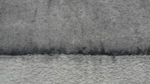 Mur en crépi gris : partie haute encrassée et microfissurée, partie basse nettoyée, la limite entre les deux est nette
