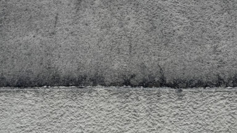 Mur en crépi gris : partie haute encrassée et microfissurée, partie basse nettoyée, la limite entre les deux est nette