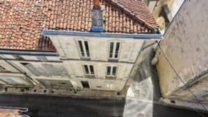 Vue aérienne par drone d’une façade en pierre de taille, de sa toiture en tuiles canal et de sa souche de cheminée, le type de relevé utilisé pour repérer fissures et désordres en hauteur