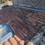 Vue aérienne par drone d'un pan de toiture en tuiles canal avec lichens, fenêtre de toit et souche de cheminée en pierre