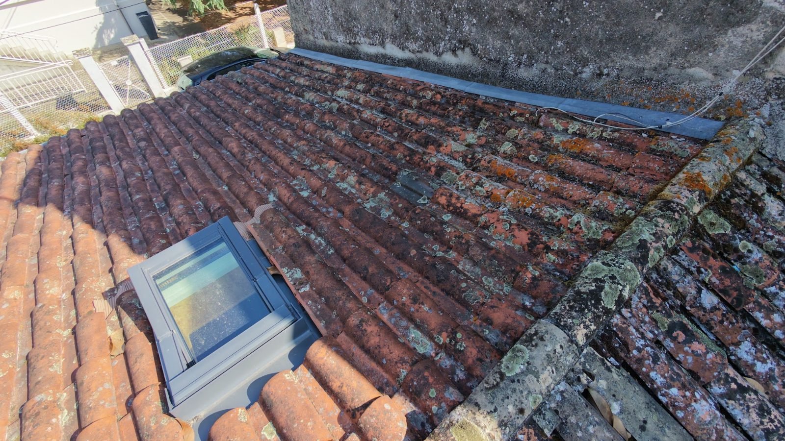 Vue aérienne par drone d'un pan de toiture en tuiles canal avec lichens, fenêtre de toit et souche de cheminée en pierre